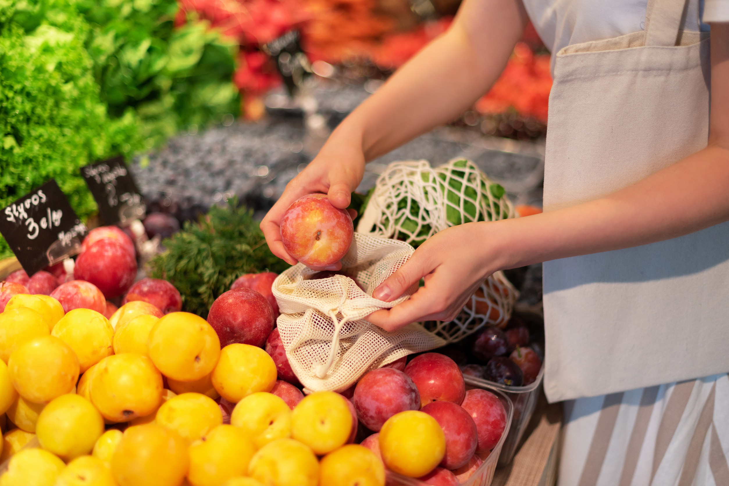Zero waste, plastic free concept. Sustainable lifestyle. Woman chooses fruits and vegetables at farmers market. Reusable cotton and mesh eco bags for shopping.