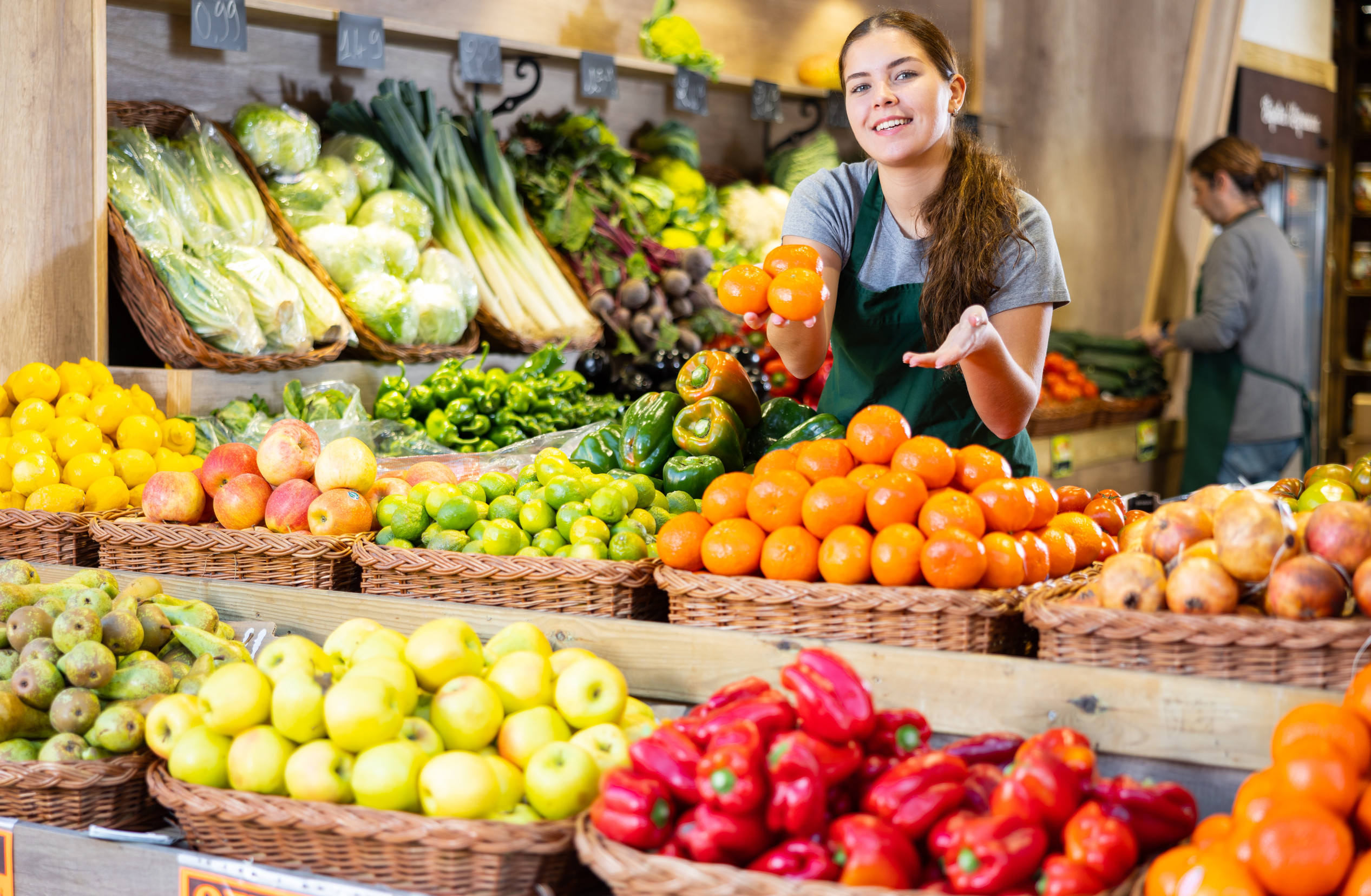 Female seller holding mandarin oranges standing in fruit and vegetable section of supermarket